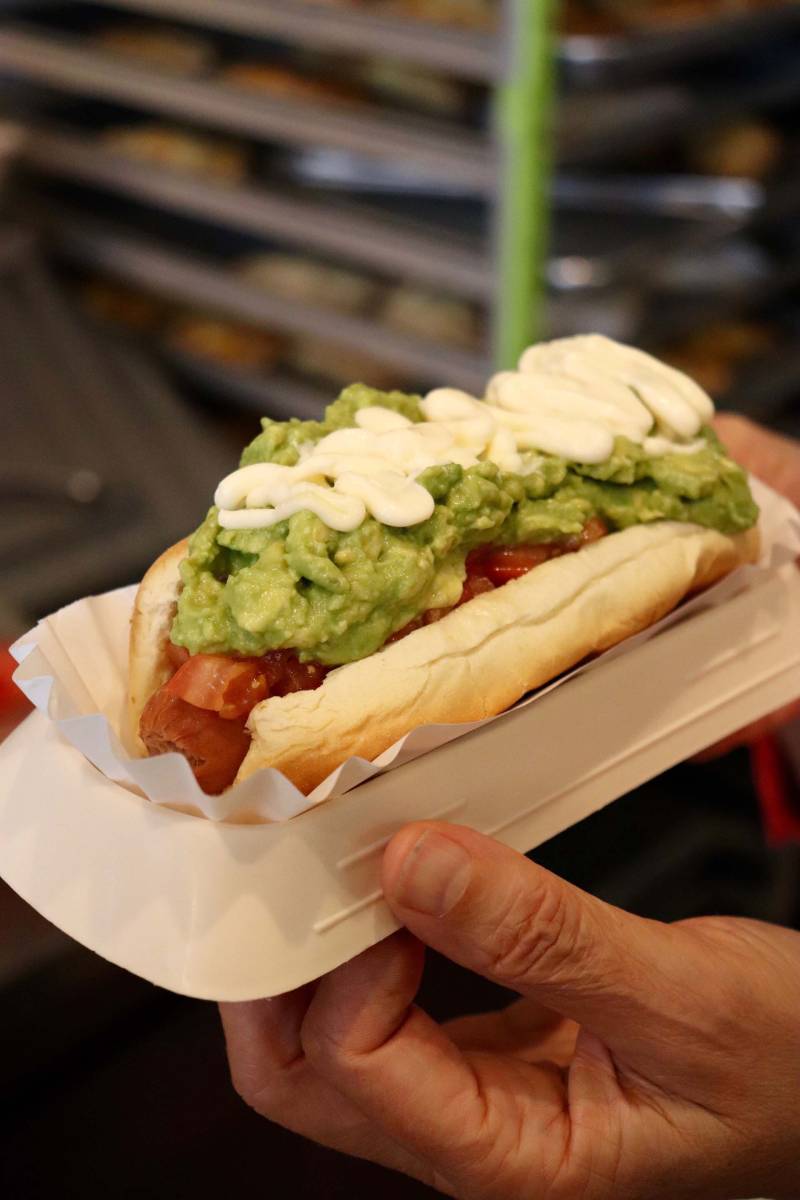A Chilean hotdog, which includes avocado, mayo, and chopped tomatoes, is held out by the foodmaker