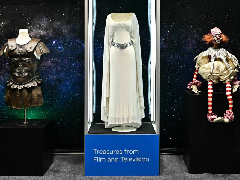 The white Princess Leia dress worn by Carrie Fisher in ‘Star Wars’ is displayed between the General Maximus armor worn by Russell Crowe in ‘Gladiator,’ and the clown doll from ‘Poltergeist.’
