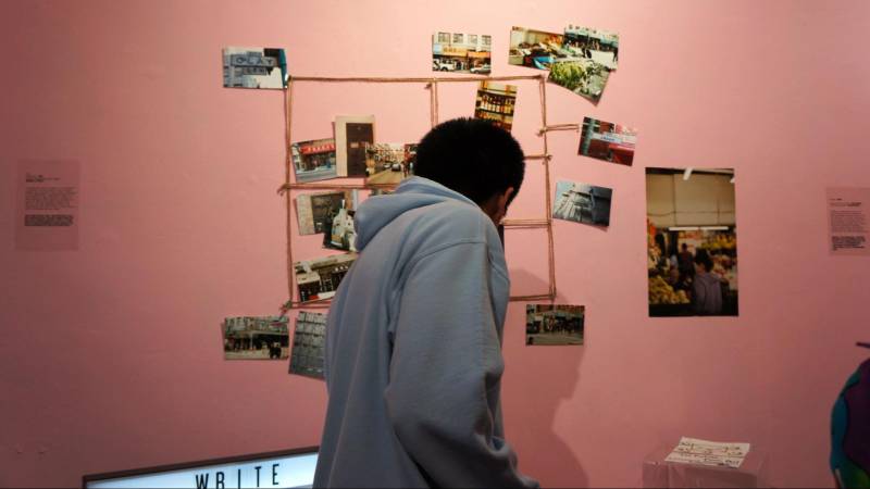 an attendee with black hair leans towards photographs posted on a pink wall
