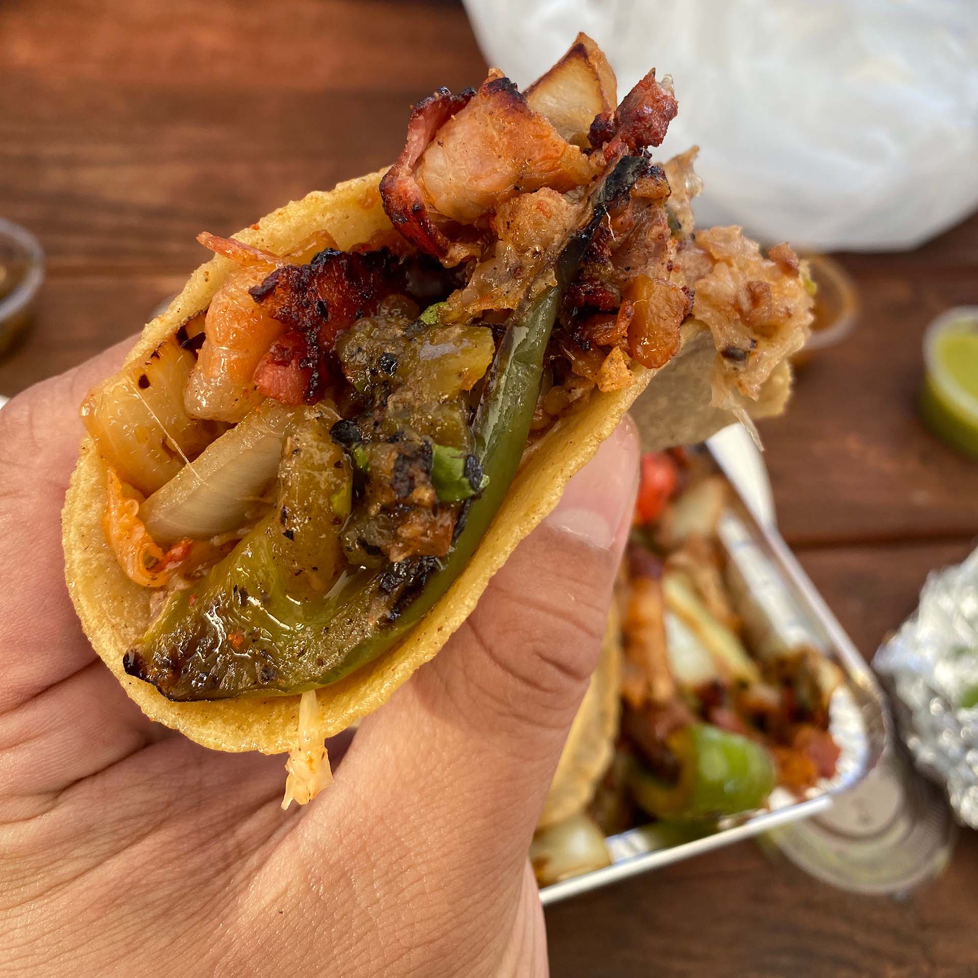 A hand holding a taco stuffed with cheesy meat, onions, and peppers.