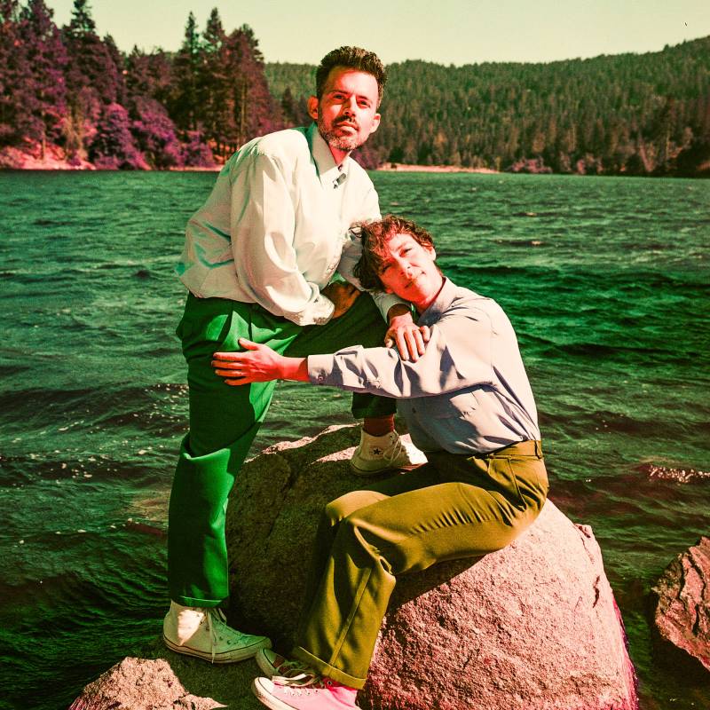 a white man and a woman pose on a rock in front of a lake