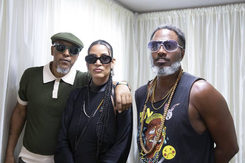 A man, a woman and another man all in their 50s pose in sunglasses.