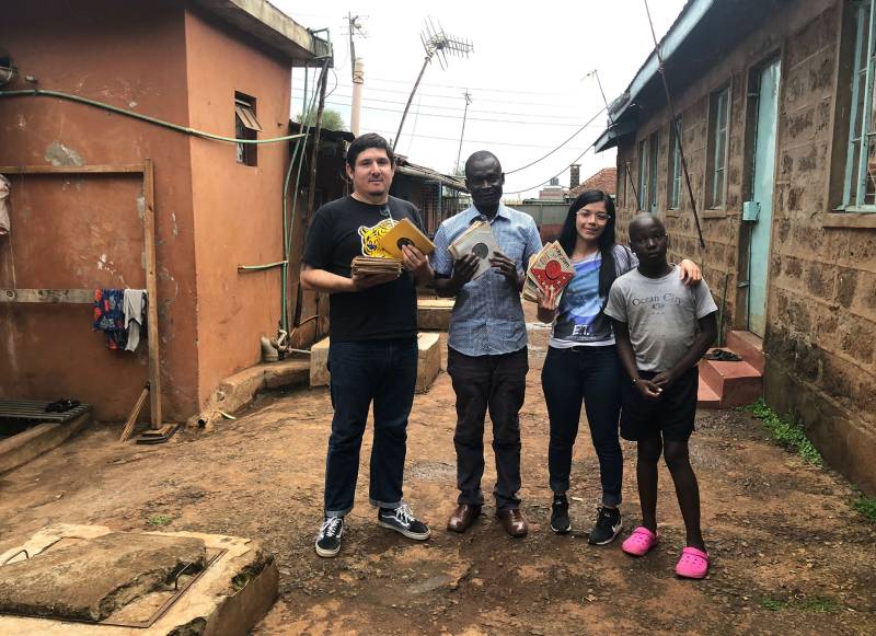 two Latinx people and two Kenyan people stand holding 45s in a village in Kenya