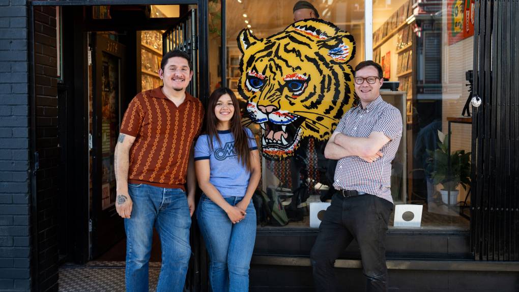 Three people in front of a window with a large tiger mural painted on it