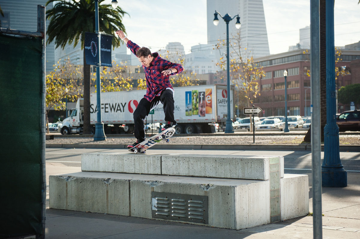 A man in a flannel shirt rides a skateboard high atop a concrete block