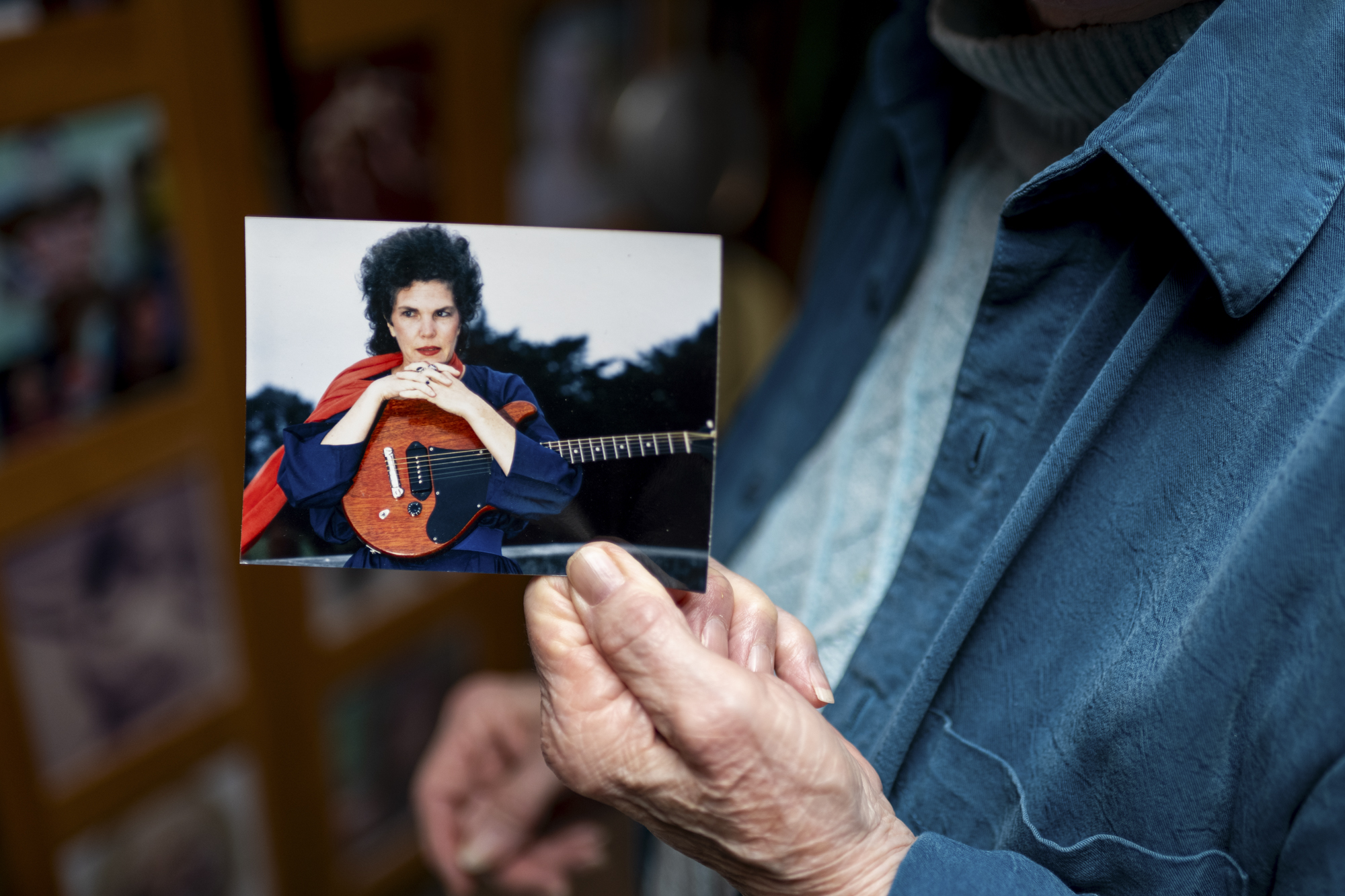 A wrinkled hand holds a photo showing a person holding a guitar.