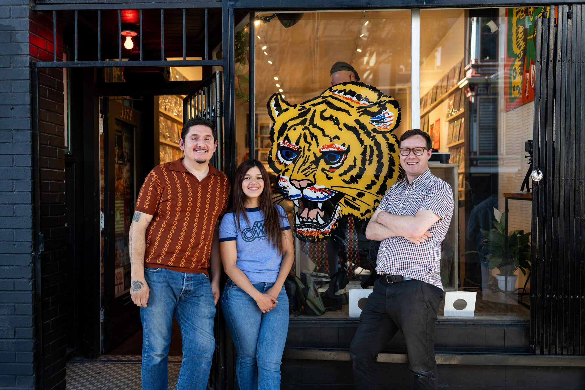 Three people in front of a window with a large tiger mural painted on it
