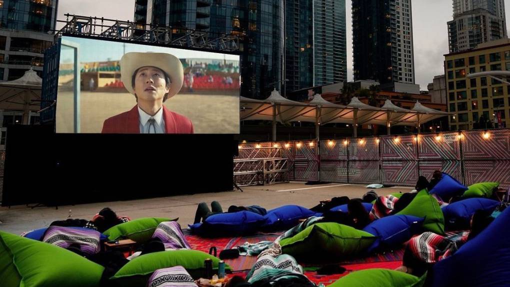 Outdoor movie screen with cowboy image and audience laying on colorful beanbags under blankets