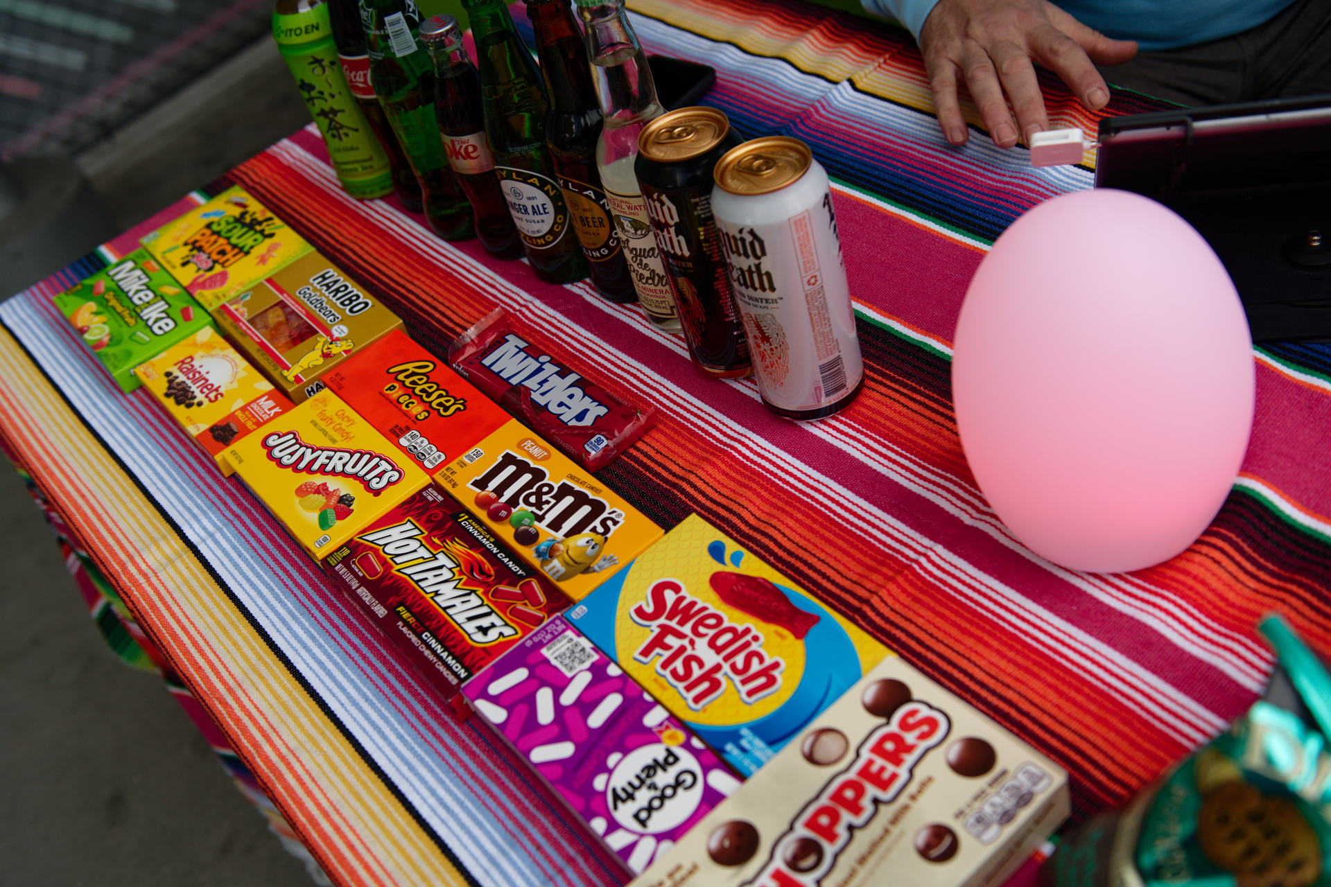Boxed candies and canned beverages displayed on a colorful Mexican blanket