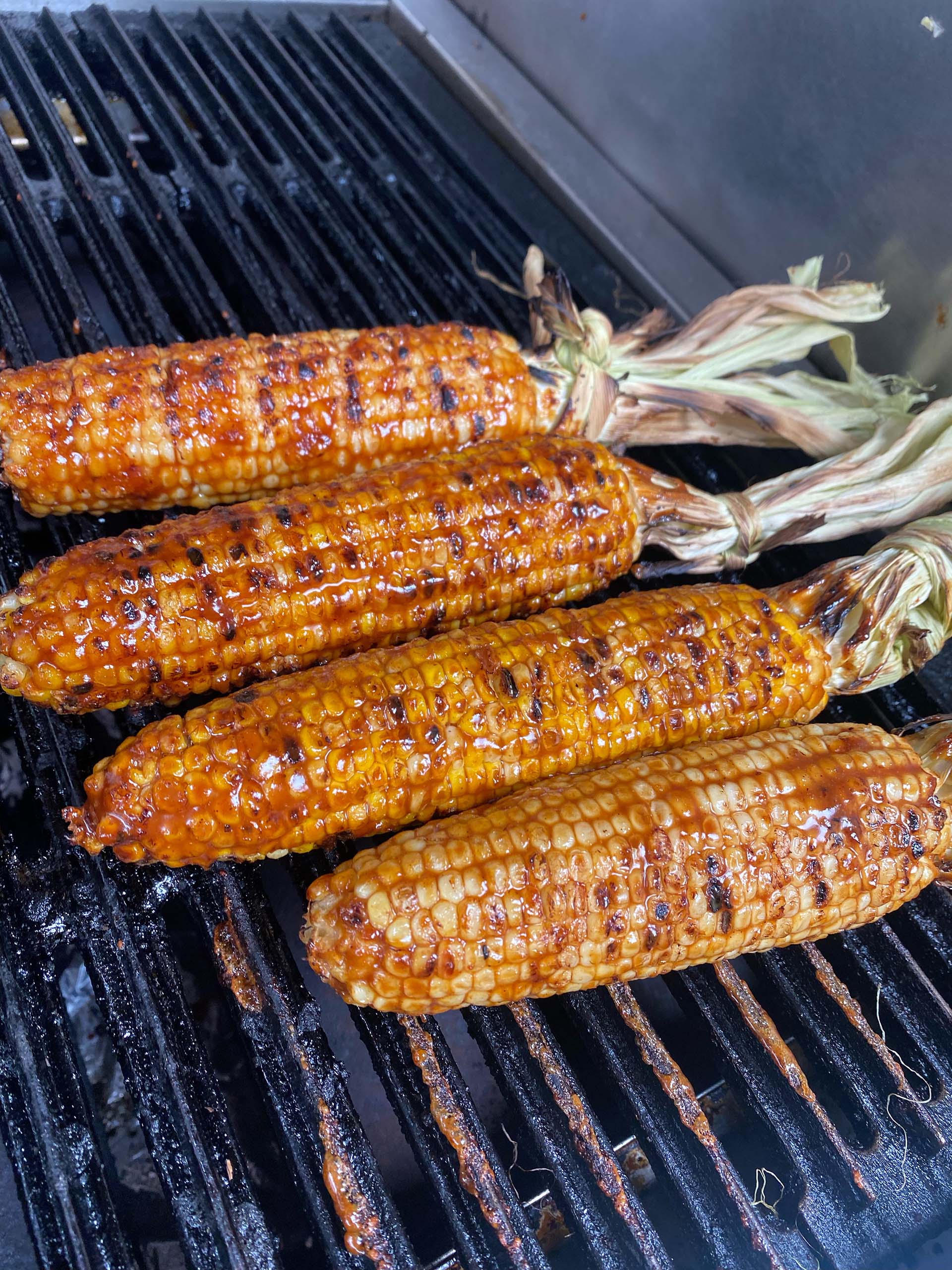 Four ears of sauce-slathered corn cook on a grill.