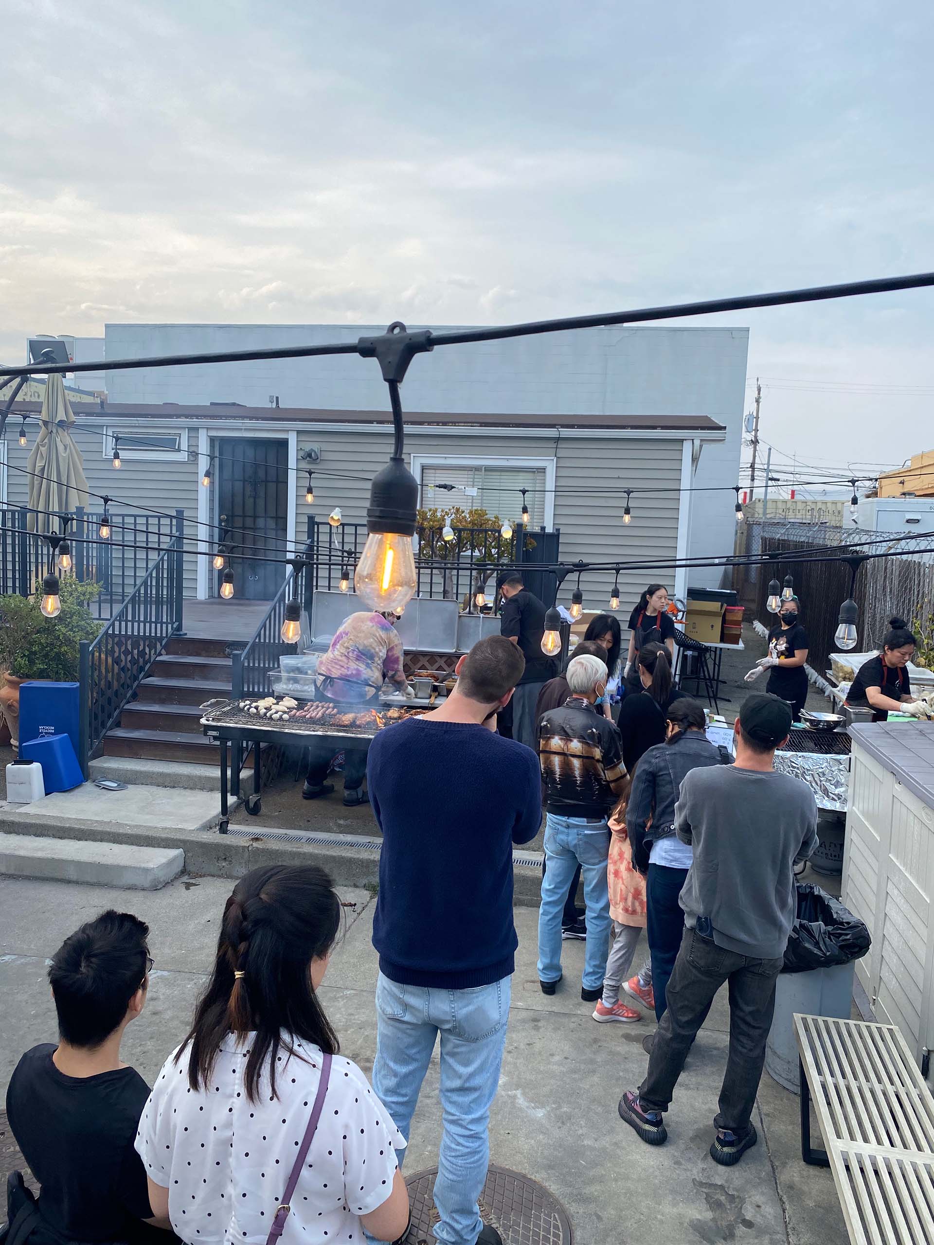 A line of customers waiting in front of a charcoal grill, where various Taiwanese barbecue items are cooking.