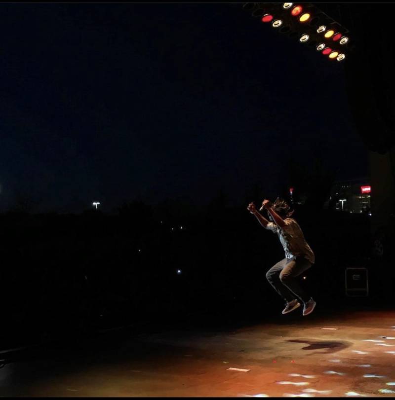 a local rapper jumps mid air while performing on a darkly lit stage