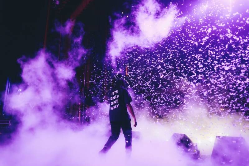 a local rapper stands on a purple lit stage while confetti falls around him