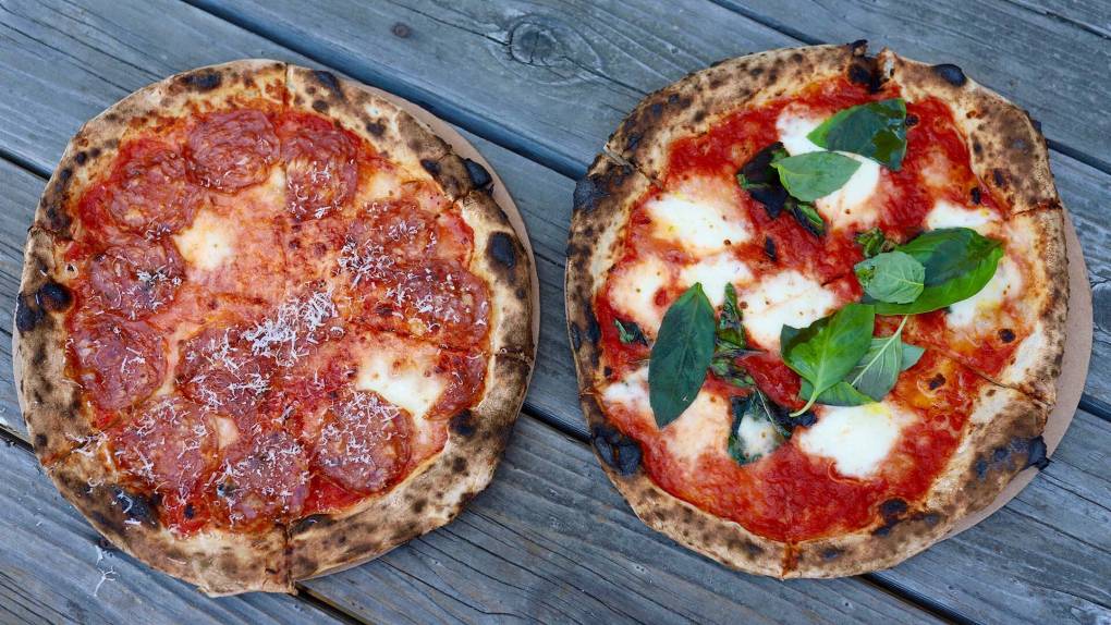 Two wood-fired pizzas on a wodden table