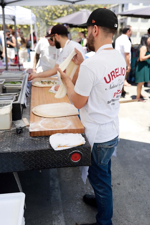 A man wearing a Urelio's Pizza shirt stretches pizza dough at an outdoor food pop-up in Berkeley