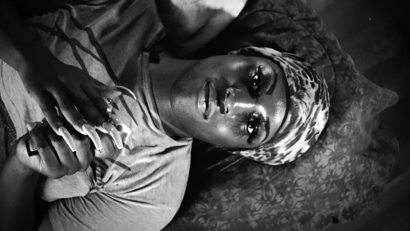 a black and white photo of a Black woman with a headscarf on, laying down looking upward at the camera