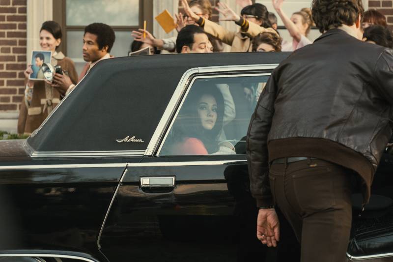 a woman with black hair looks out the window of a limo in a crowd of people
