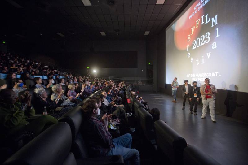 four people on a stage at a film festival in front of a packed theater