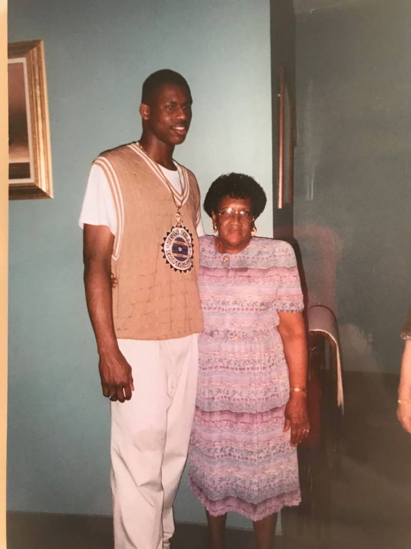 an NBA player stands next to his grandmother in a living room