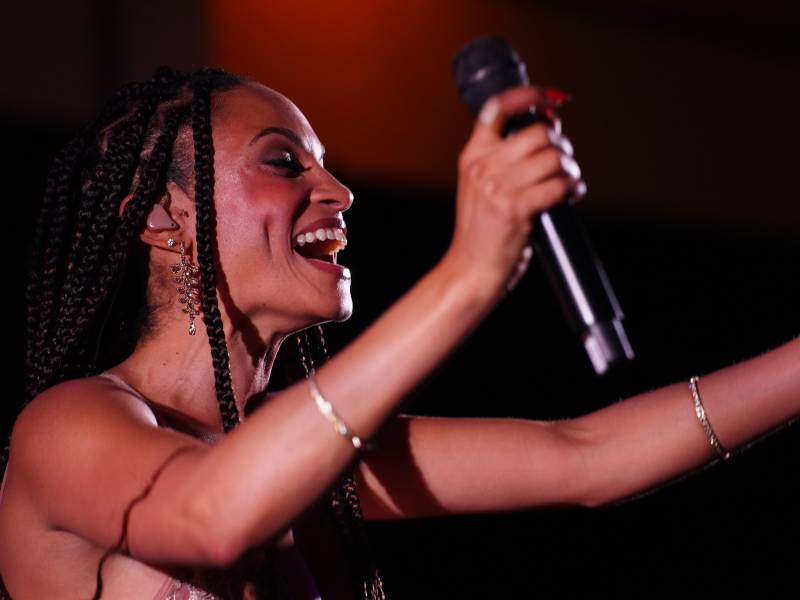 a Black woman with braids smiles holding a microphone on stage