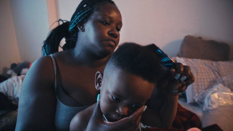 a Black woman with braids combs her toddler son's hair
