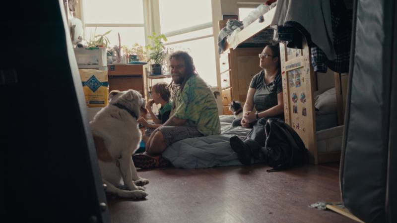 three white people sit on the floor of a small room with a dog