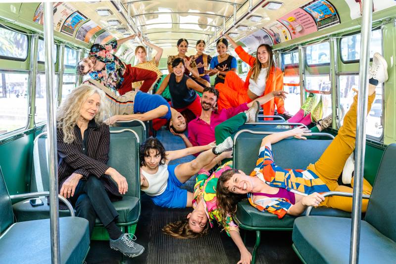 a group of dancers in colorful clothes pose inside a trolley with green seats