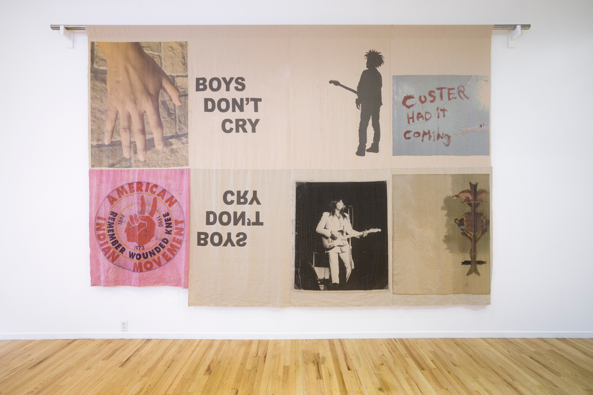 Hanging textile with patchwork of images of bands and slogans like "boys don't cry" and "Custer had it coming"