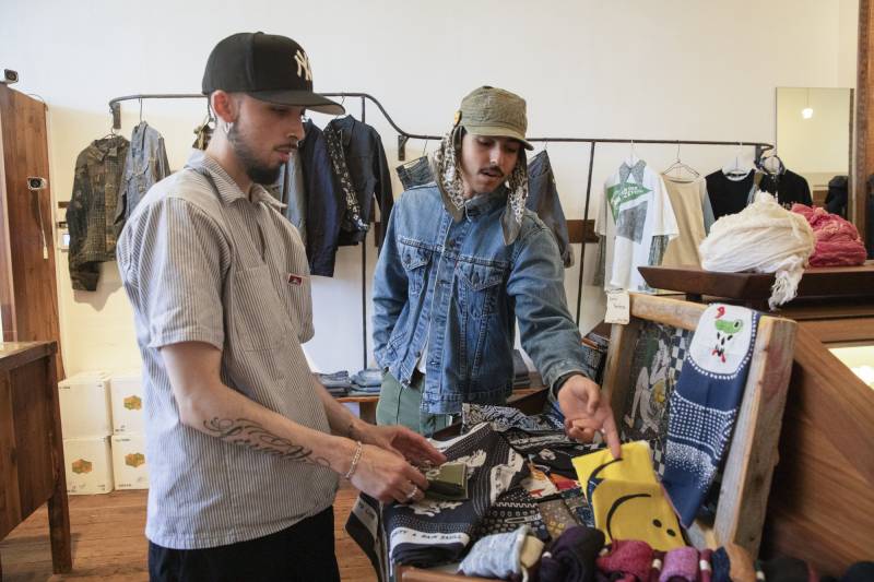 Two people wearing hats looks at wares in a modern-looking clothing store.