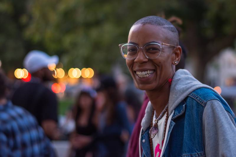 A black woman with short hair and glasses smiles at the camera.