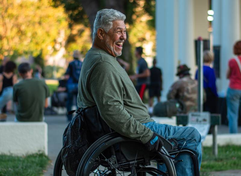 A man sits in a wheelchair while smiling widely.