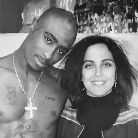 A shirtless black male with a cross necklace stands with a shorter white woman in jeans and striped top.