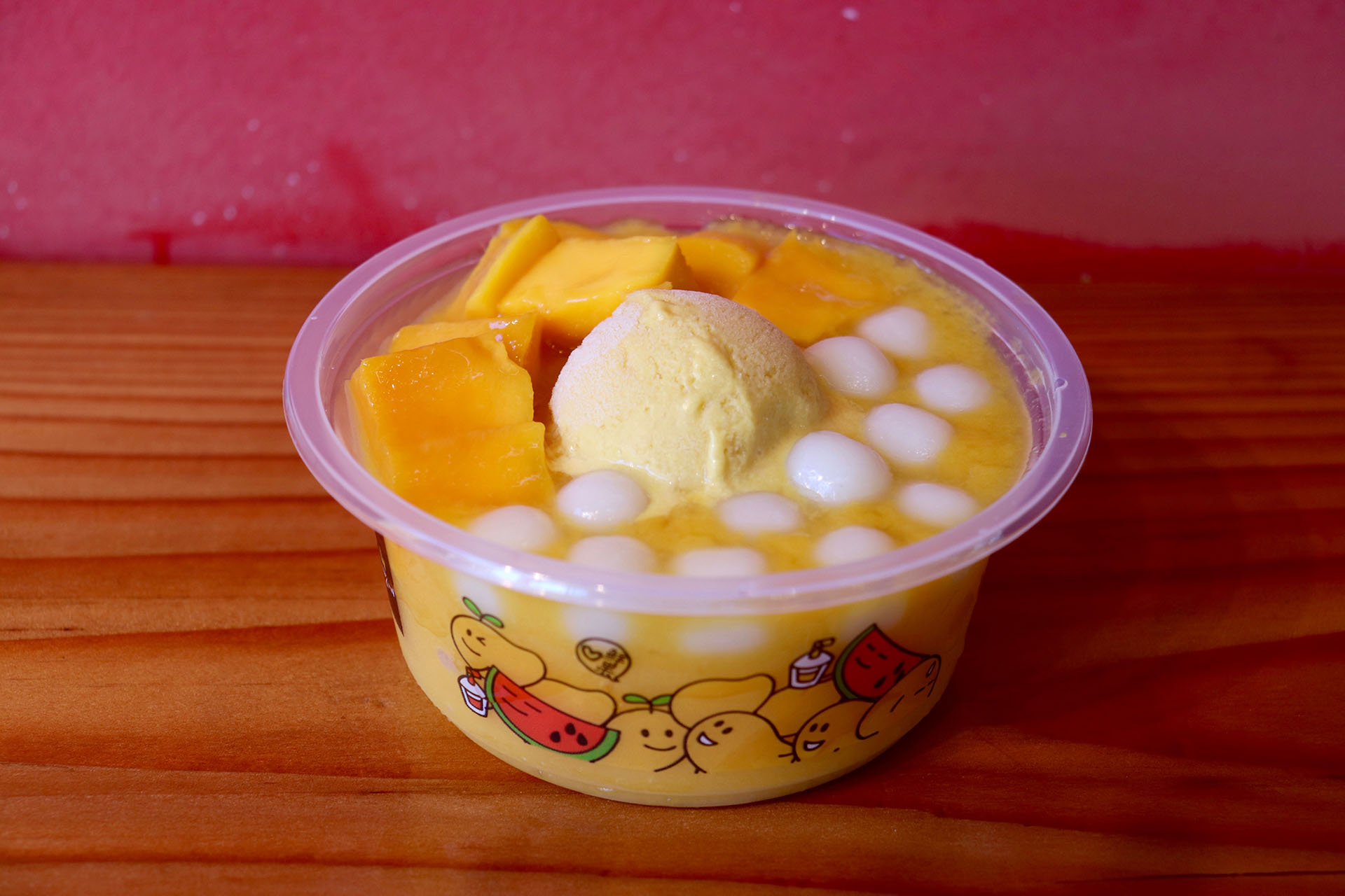 a cold dessert dish that includes mango sorbet, mango chunks and mochi-like balls on a wooden counter