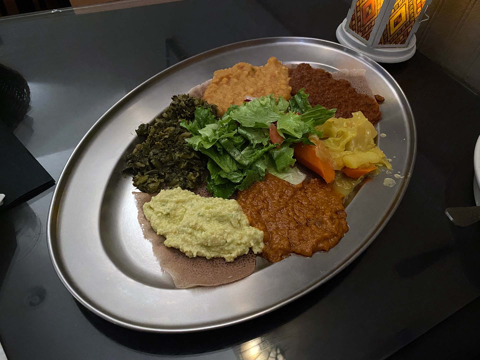 An Ethiopian veggie combo: six colorful spreads dolloped on an injera-lined metal plate.