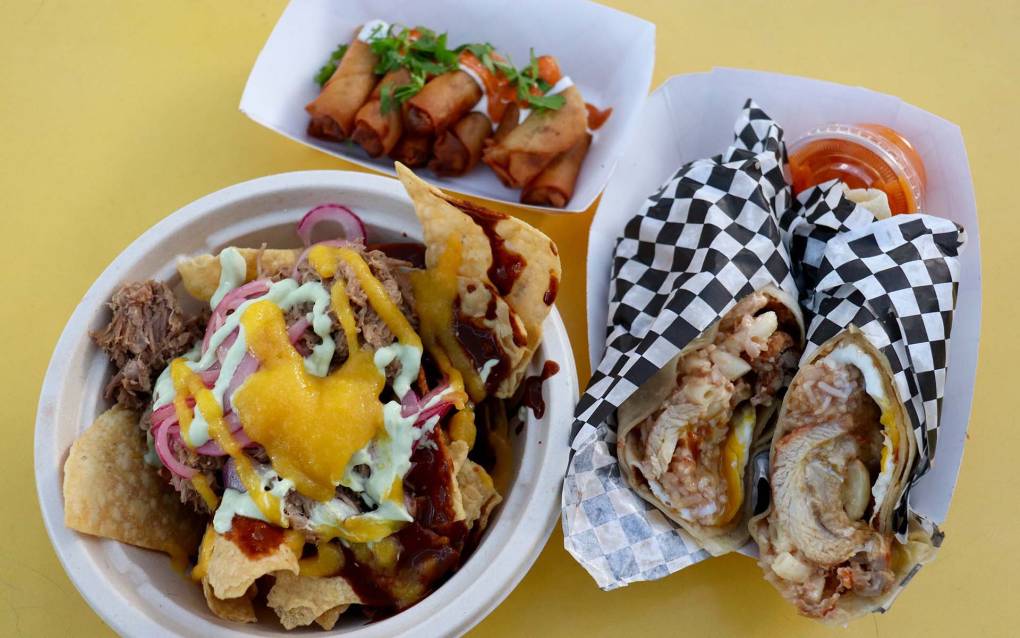 a burrito, chilaquiles, and lumpia are showcased on a yellow table outdoors