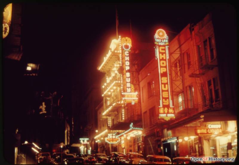 A street at night, lit up by neon signs, two of which say CHOP SUEY.
