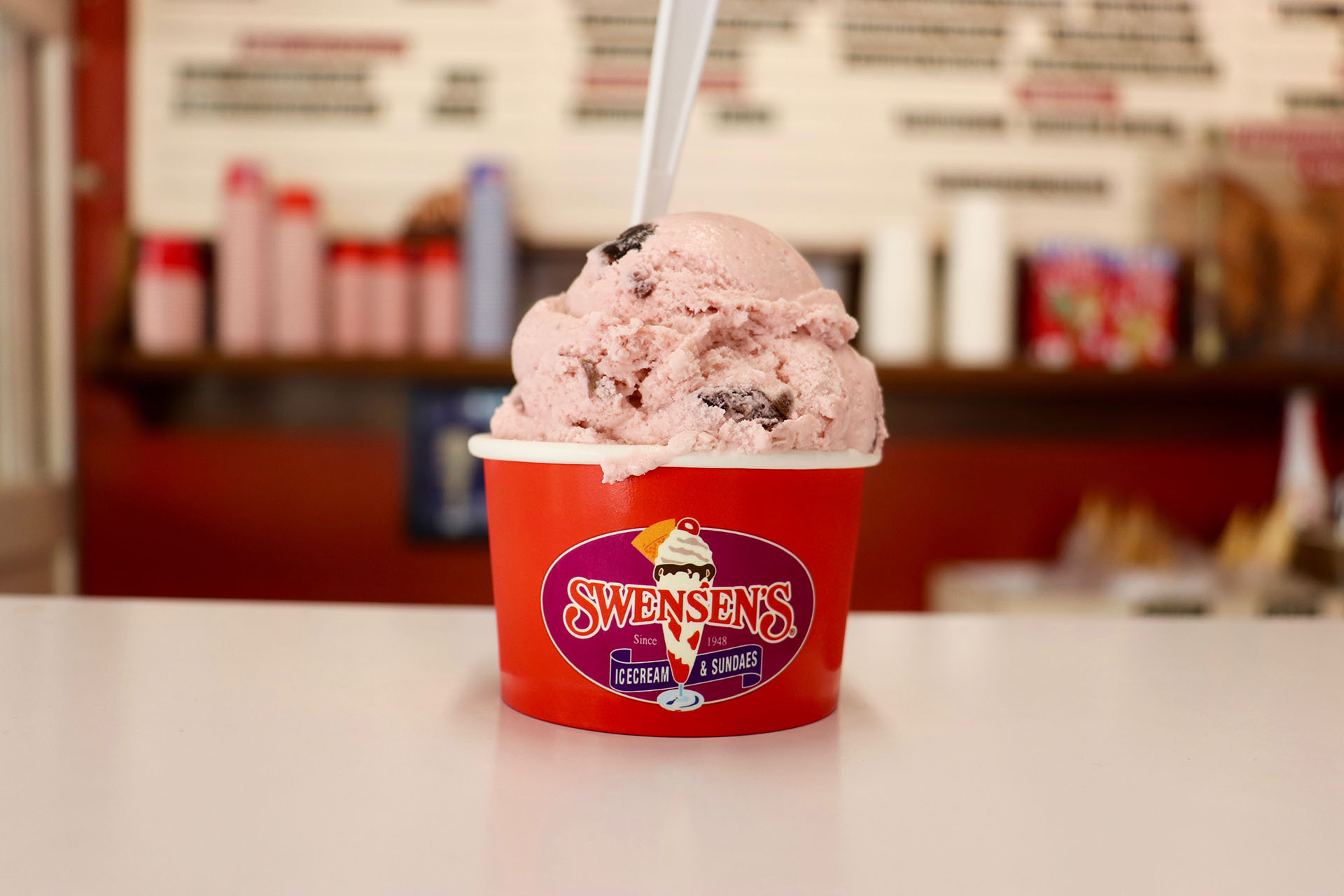 a generous scoop of cherry ice cream on a white counter inside an ice cream parlor