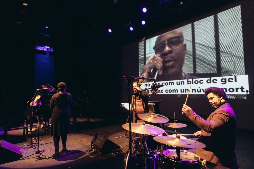 A jazz band plays live on stage while a video projection shows Keith LaMar reading spoken-word poetry from prison.