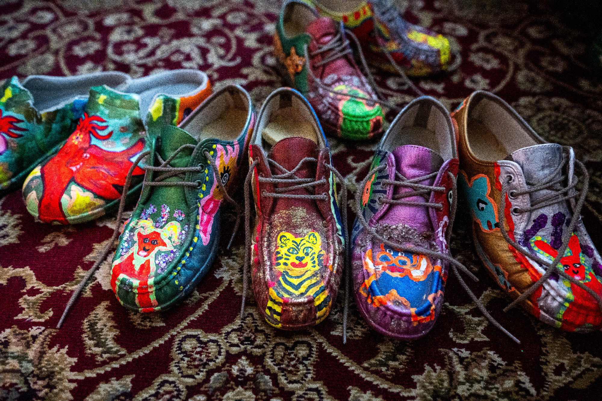 Eight shoes with painted animal designs on the toes on a patterned rug
