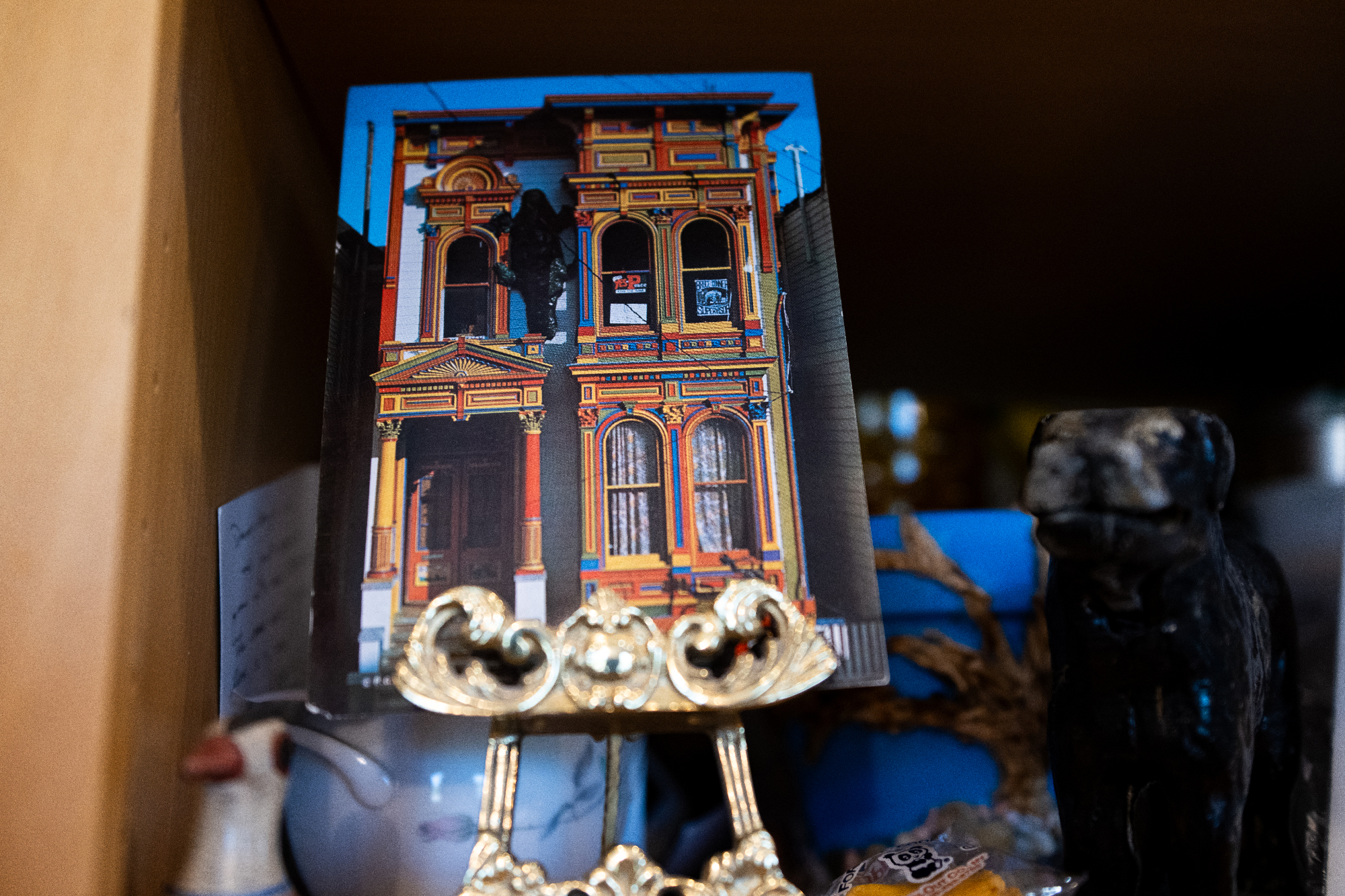Postcard of brightly painted Victorian house held in a metal clip on a shelf of knickknacks