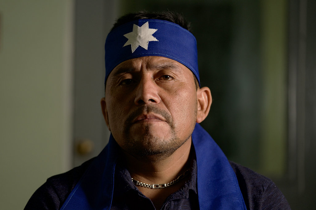 A brown-skinned man in a blue head wrap with a white eight-pointed star stitched to its center