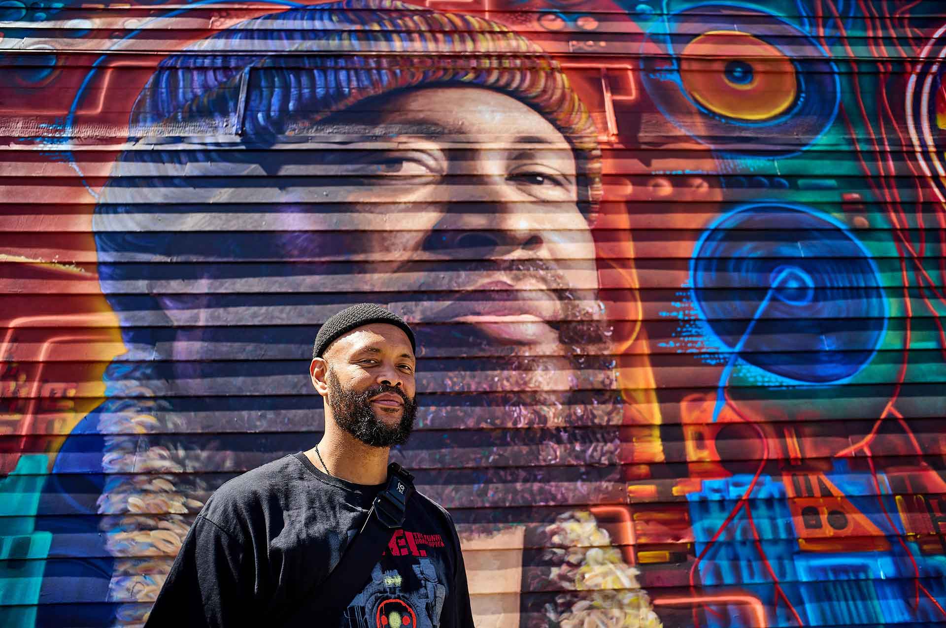 Tajai of Souls of Mischief poses in front of his own likeness, painted as part of a mural in East Oakland.