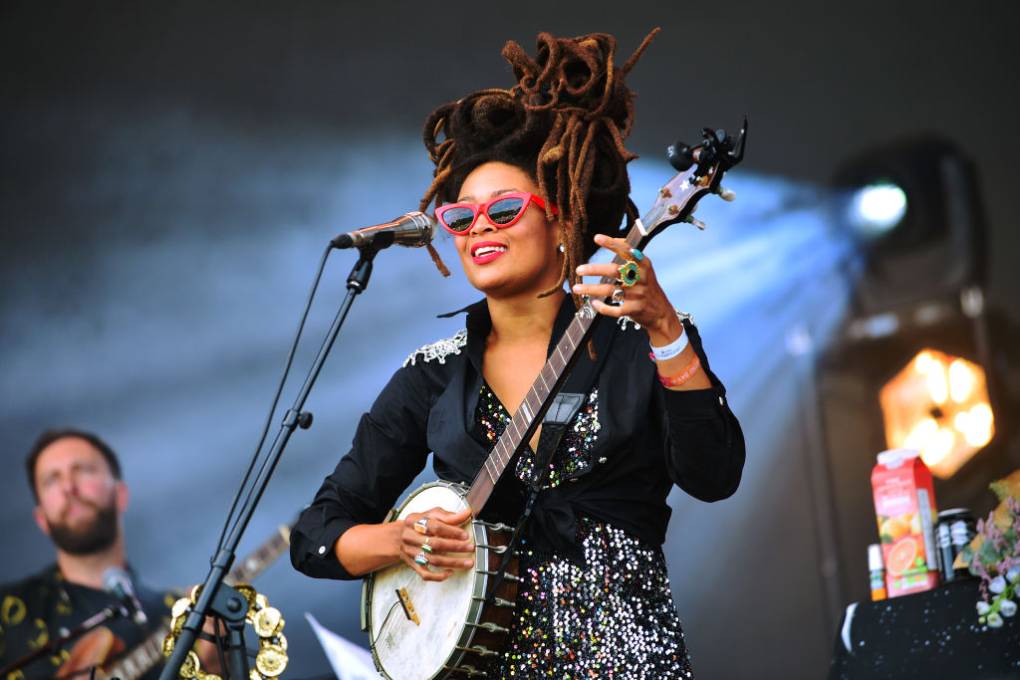 Valerie June strums a banjo on stage while wearing sunglasses.