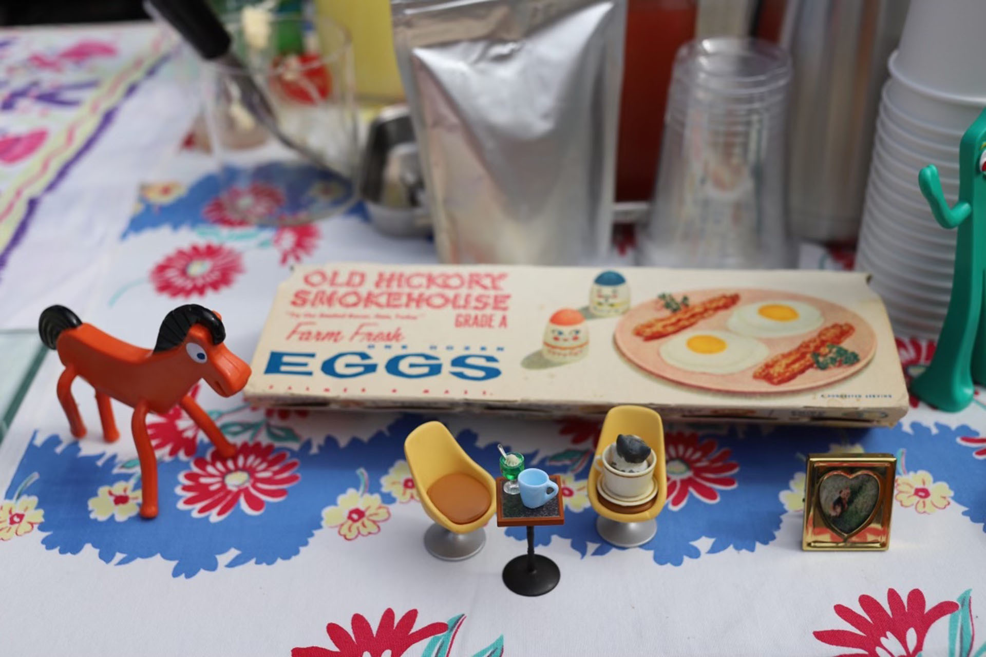 a collection of antique knick-knacks are playfully laid out on a table next to a hand painted sign that reads “eggs”