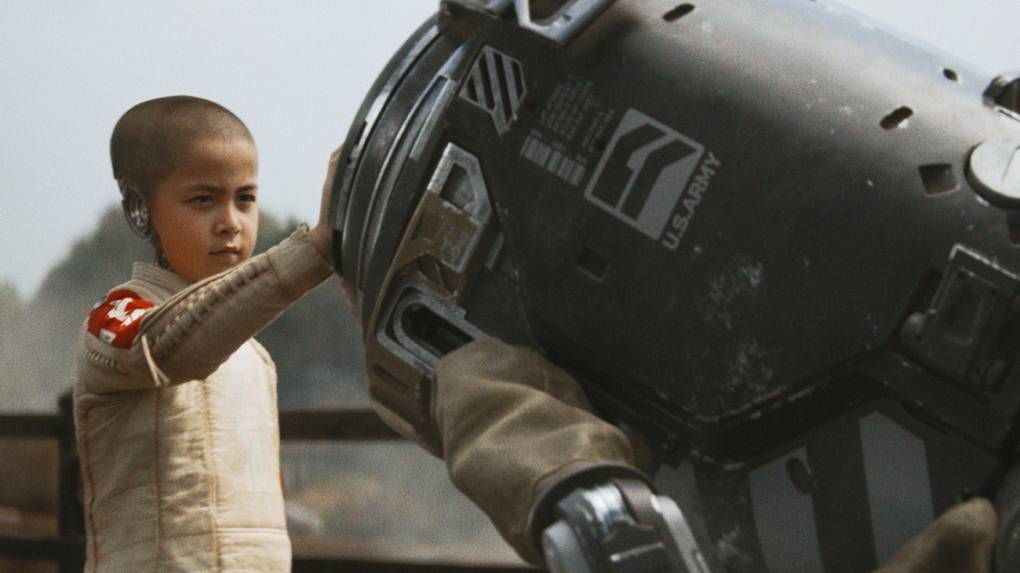 A young Asian child with a shaved head touches a large piece of mechanical equipment that has US Army written on the side of it.