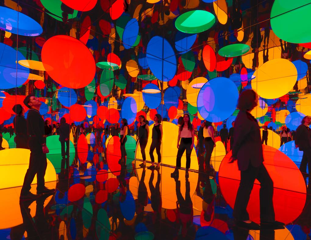 People in a mirrored room with red, blue, green and yellow circles reflected all around