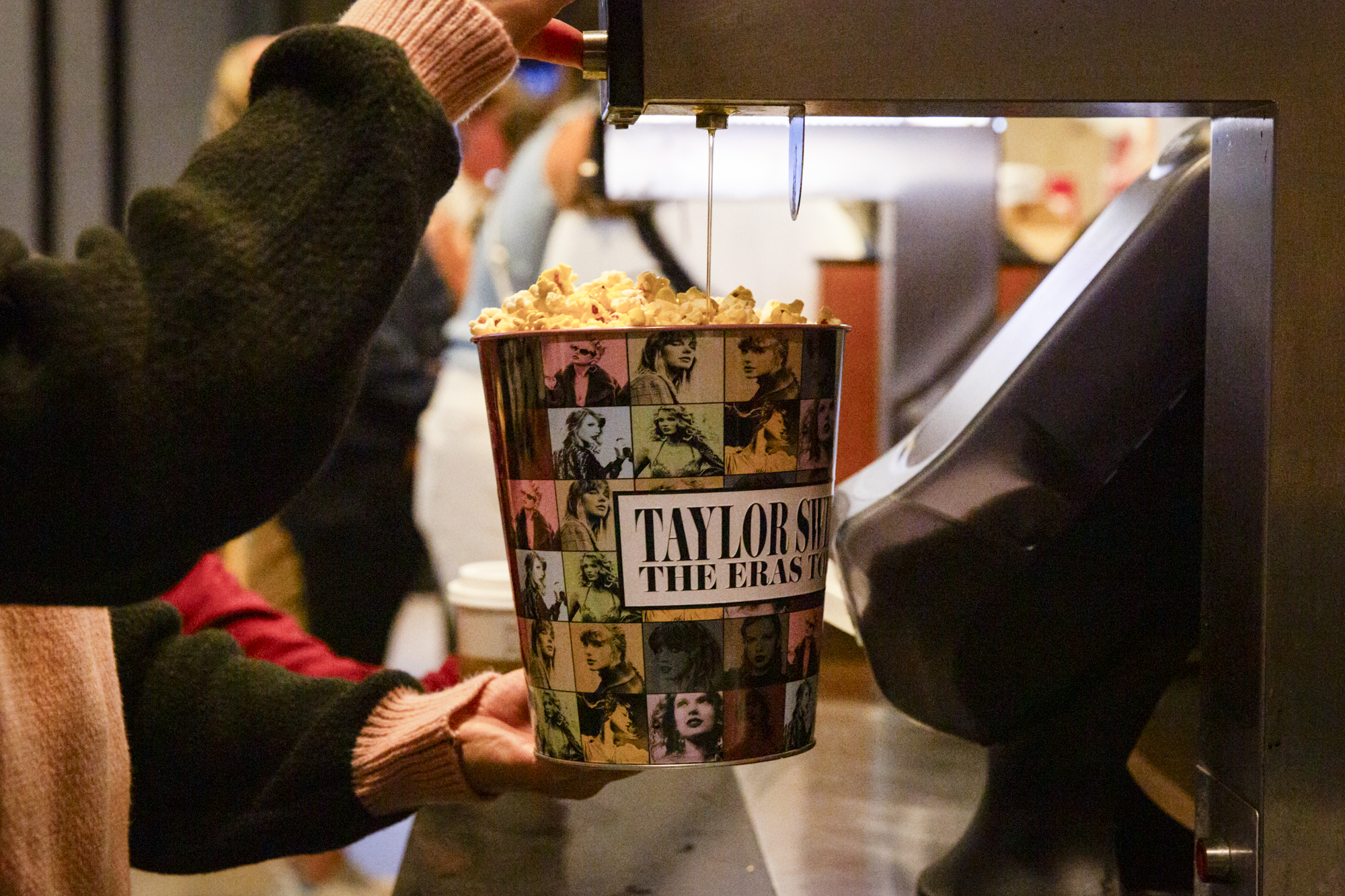 Movie theater butter is drizzled over a large tub of popcorn with photos of Taylor Swift on it.