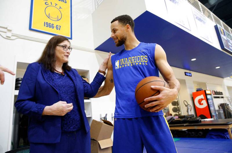 A woman in blue with long brown hair and glasses talks with a man in blue athletic gear