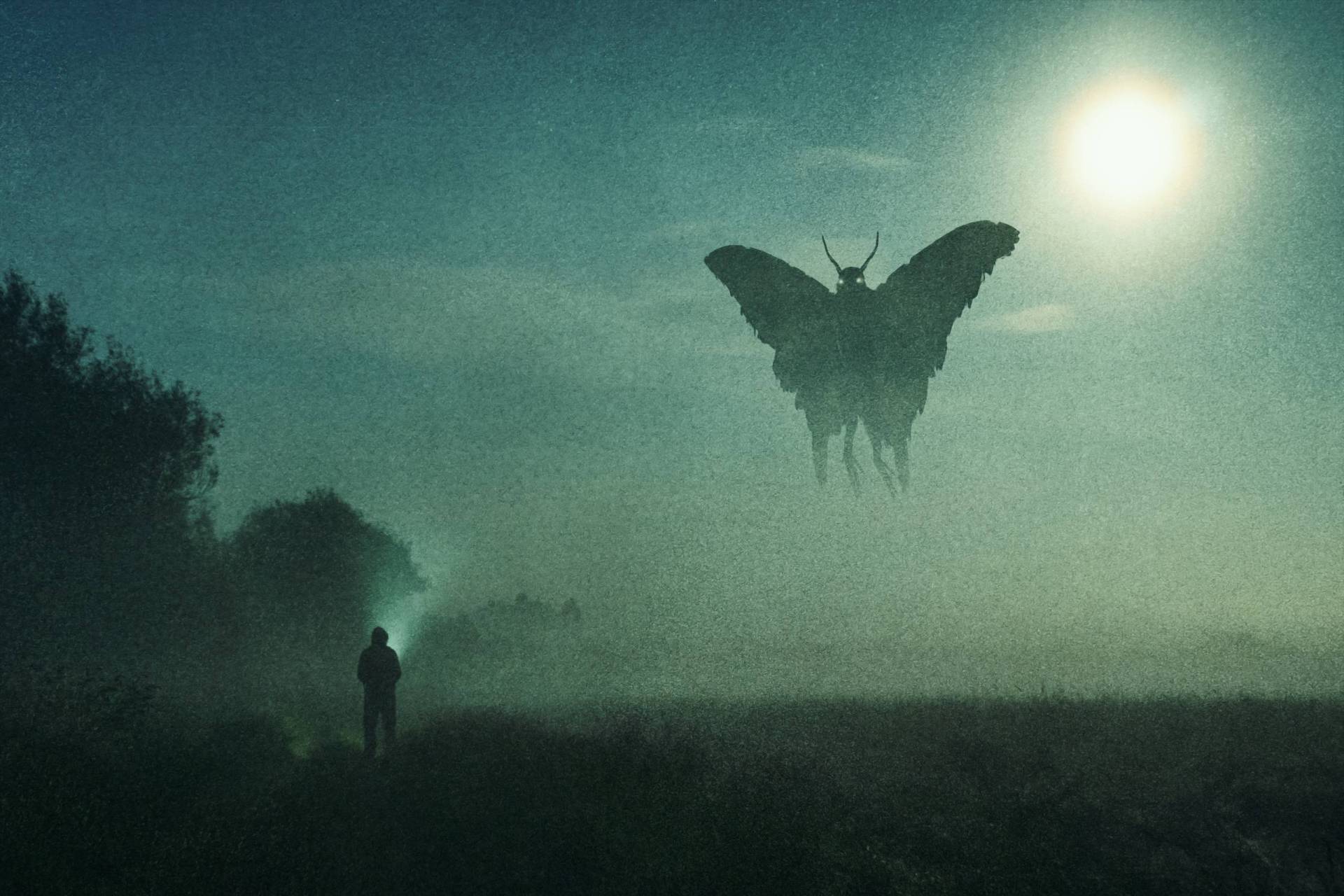 A man looks up at a flying mothman figure in the sky that's silhouetted against the moon at night.