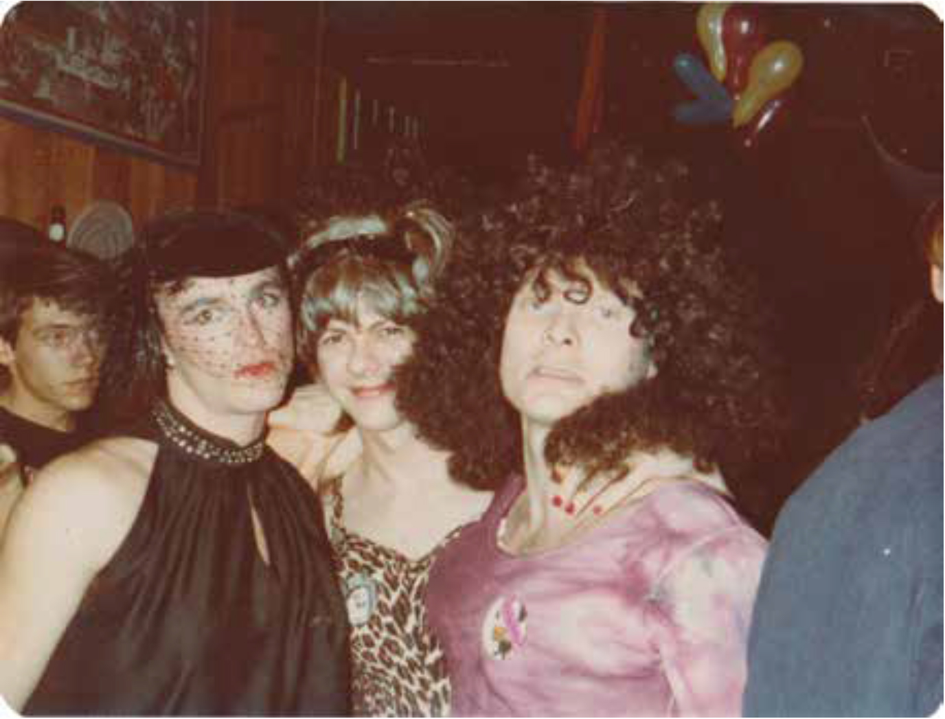 Three white people pose in fancy dress and makeup at a party